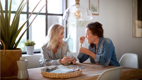 To kvinder taler i et hjem under en Philips pære