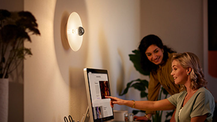 Kvinde arbejder på en computer ved siden af en vægmonteret Philips LED spejl pære