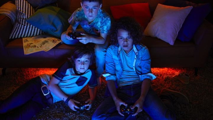 Tre drenge spiller computerspil med stemningsfuldt lys