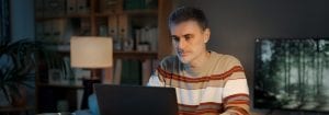 En mand iført en stribet trøje sidder ved sit skrivebord og kigger på den bærbare computer foran sig