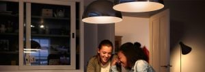 To piger, der sidder og snakker ved et spisebord, oplyst af en pendellampe med en energieffektiv LED-pære.